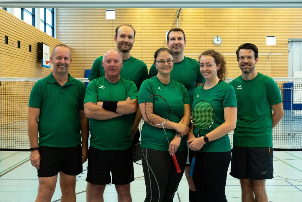 Auf dem Foto ist die Erwachsenenmannschaft der Badminton Gemeinschaft Grünau abgebildet. Von links nach rechts stehen Tino, Jochen, Raphael, Jessica, Thomas, Janita und Christian. 